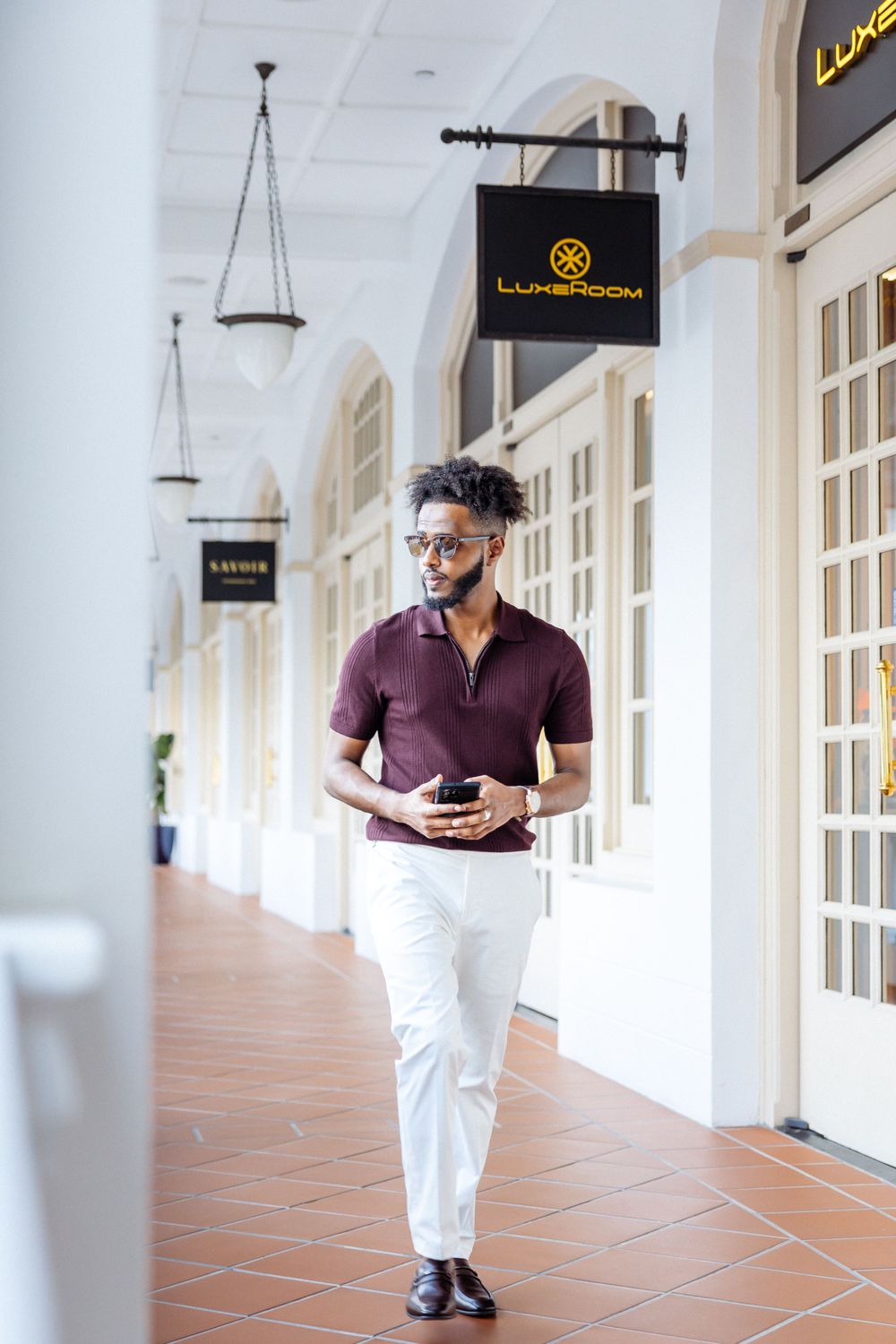 Man in burgundy polo walks confidently along colonial-style corridor with hanging shop signs.