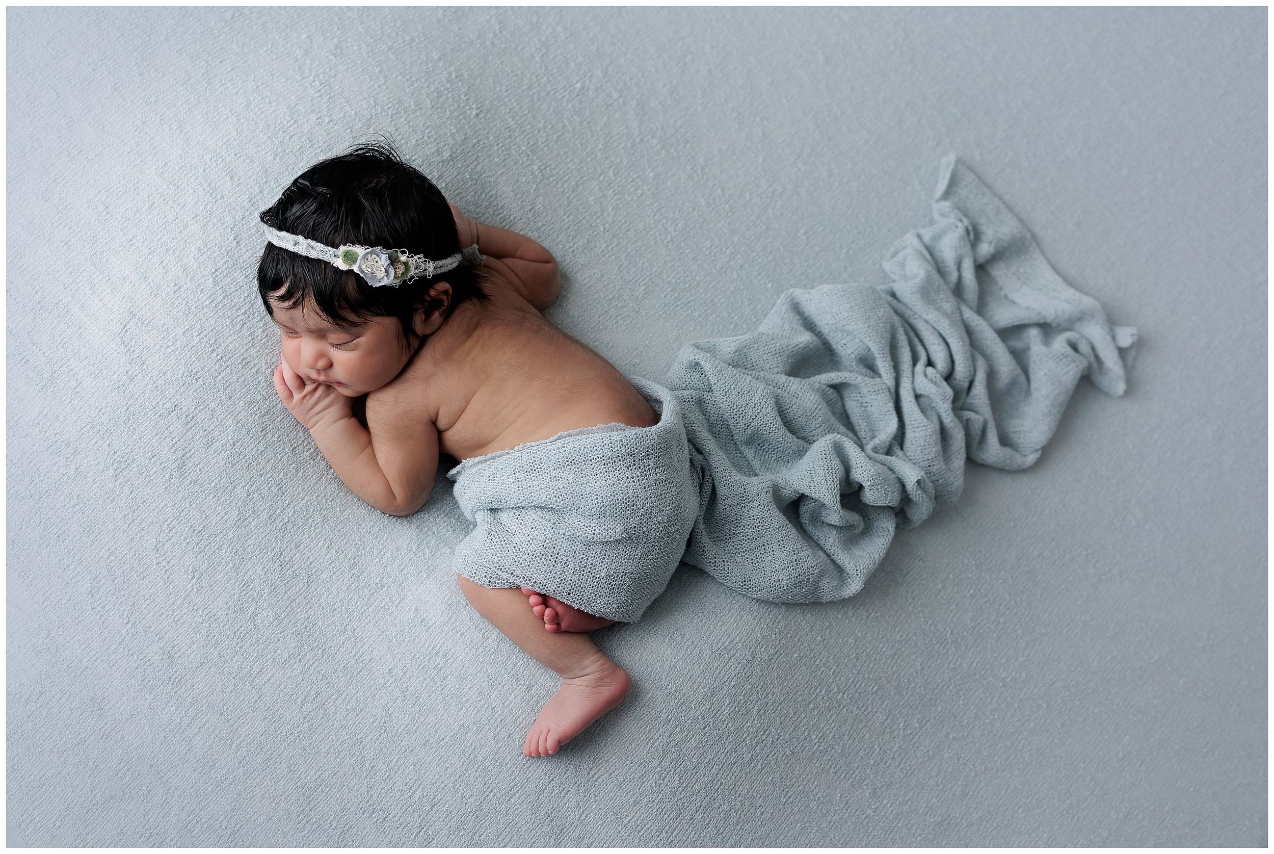 Newborn baby lying on soft blue fabric backdrop during studio newborn session in North Austin