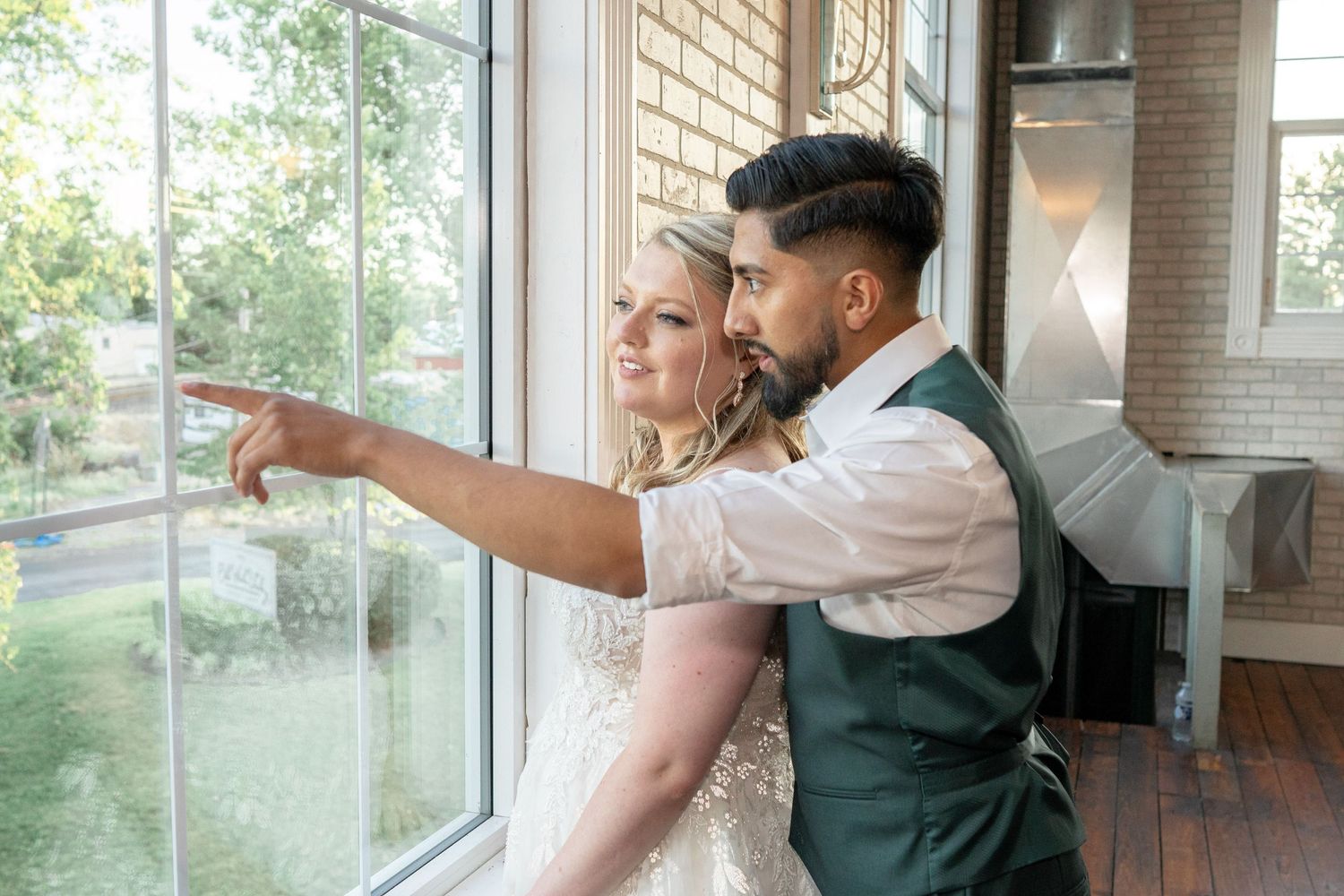 A couple in wedding attire gazes out a large window together.