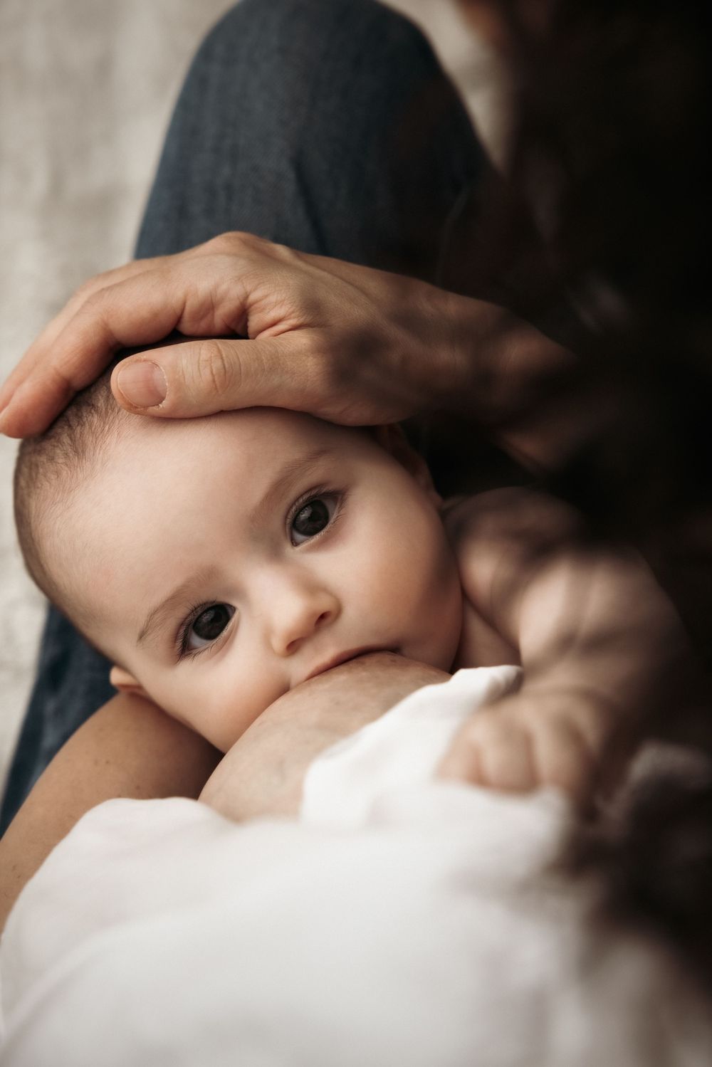 A sweet baby in closeup side view with expressive eyes gazes at the camera while being held by parent.