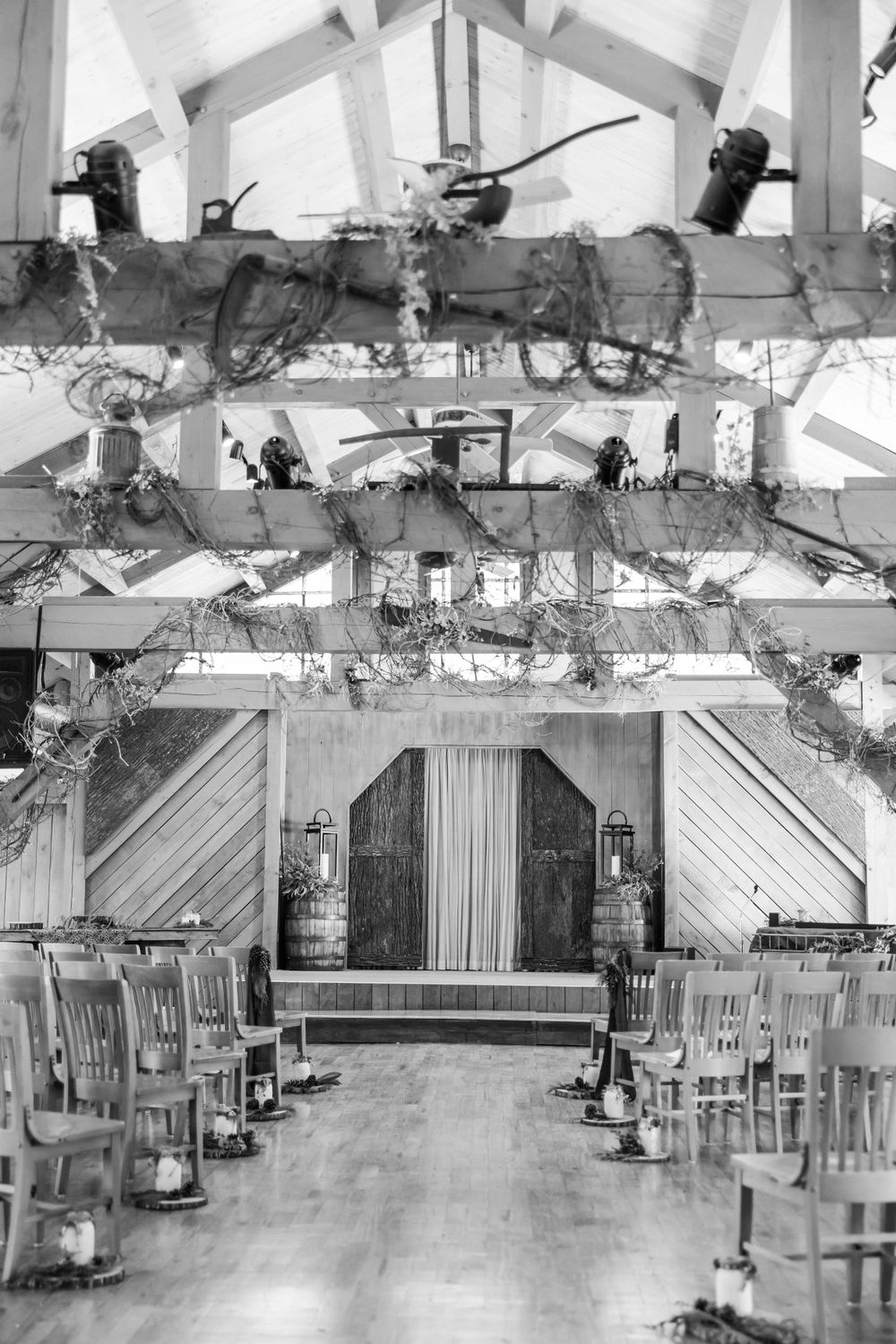 Black and white photo of a rustic wedding venue interior with decorated beams and wooden chairs.