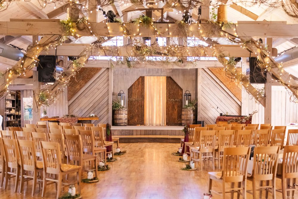 Rustic barn wedding venue with wooden chairs lined up for ceremony and golden garland decorations on exposed beams.