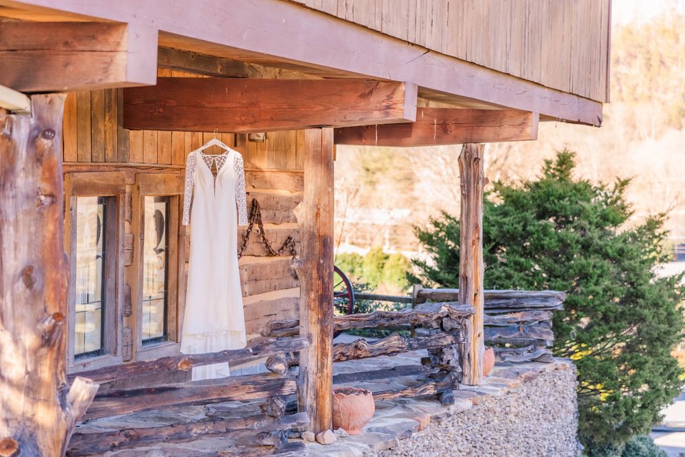 White wedding dress hanging on rustic wooden porch of log cabin.