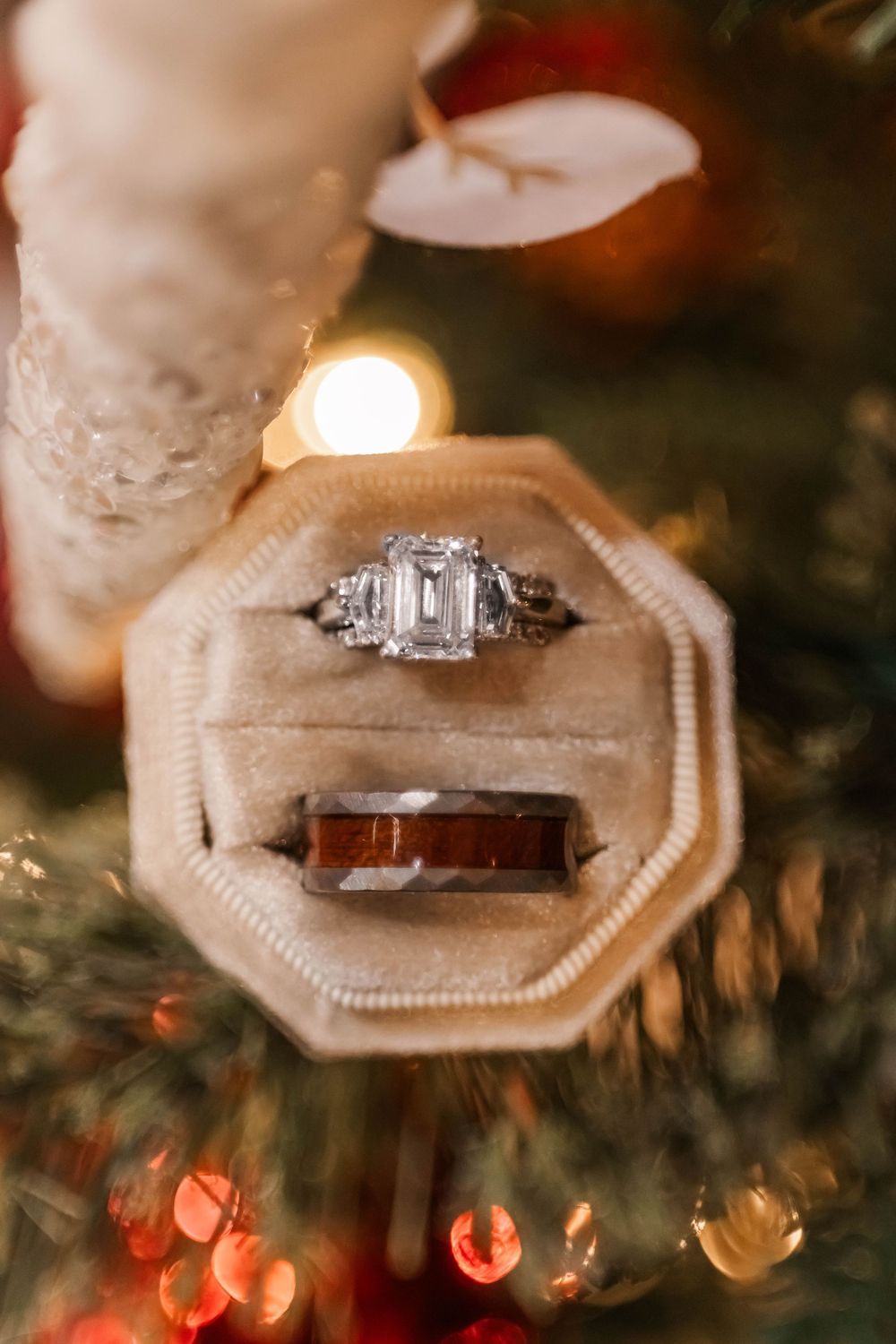 Diamond engagement ring and wedding band displayed in octagonal box against holiday lights.