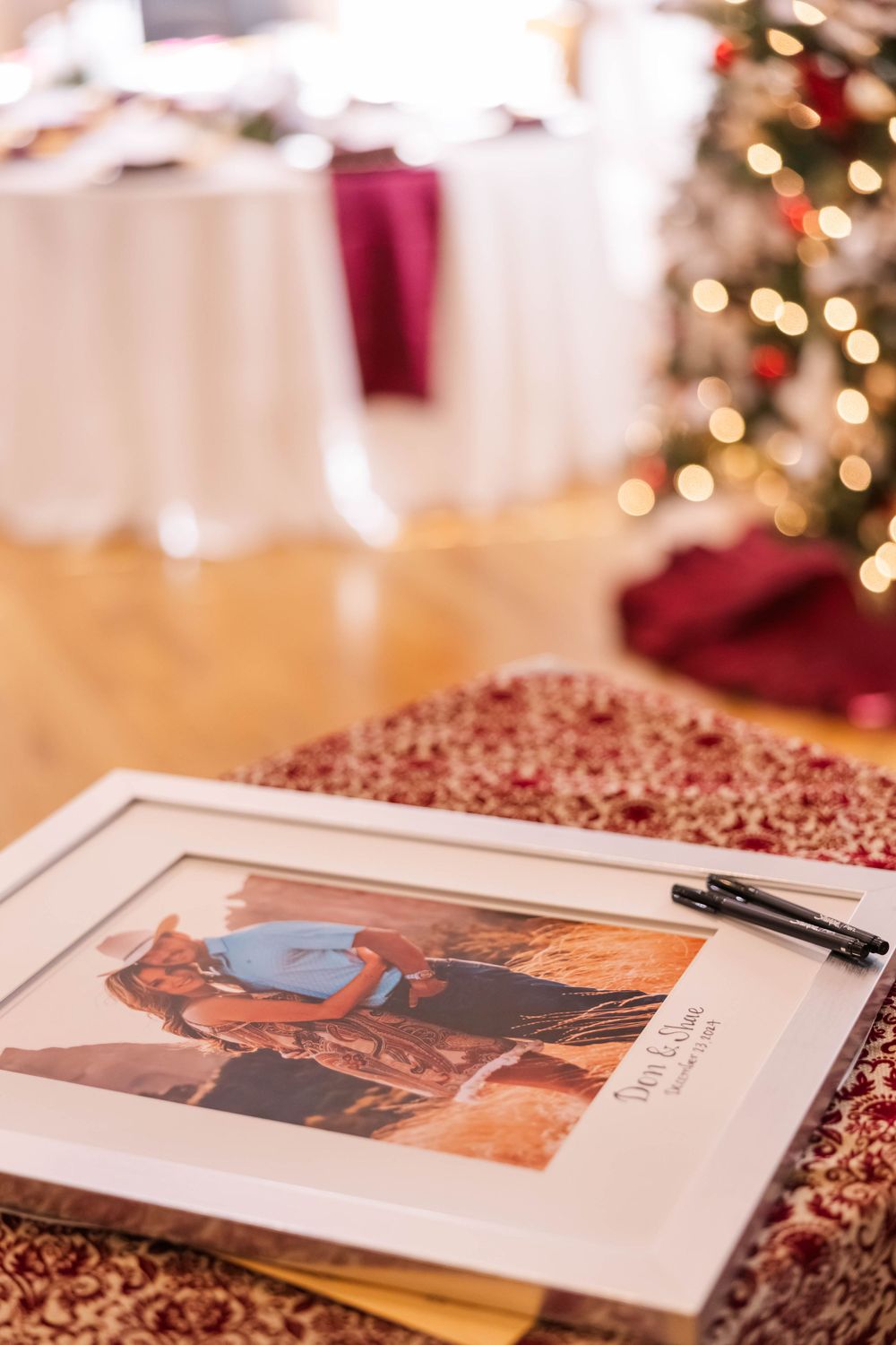 A framed photo on a sparkly burgundy tablecloth with Christmas lights in the background.