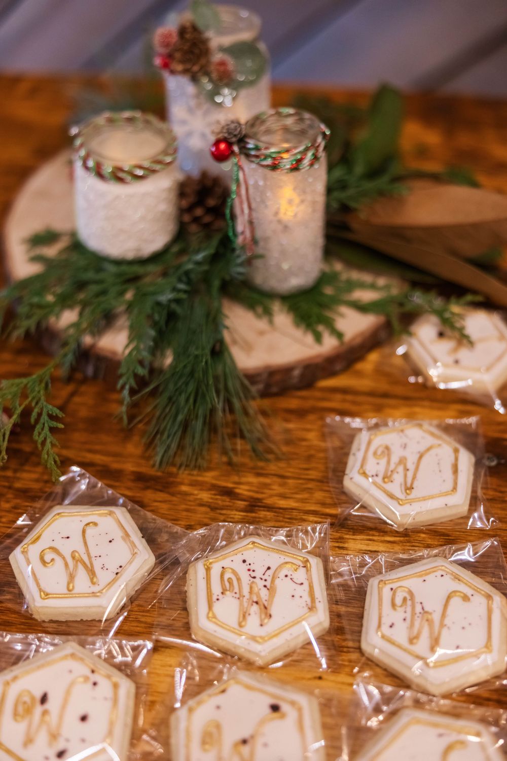 Decorated mason jar candle holders with monogrammed cookies displayed on wooden surface.