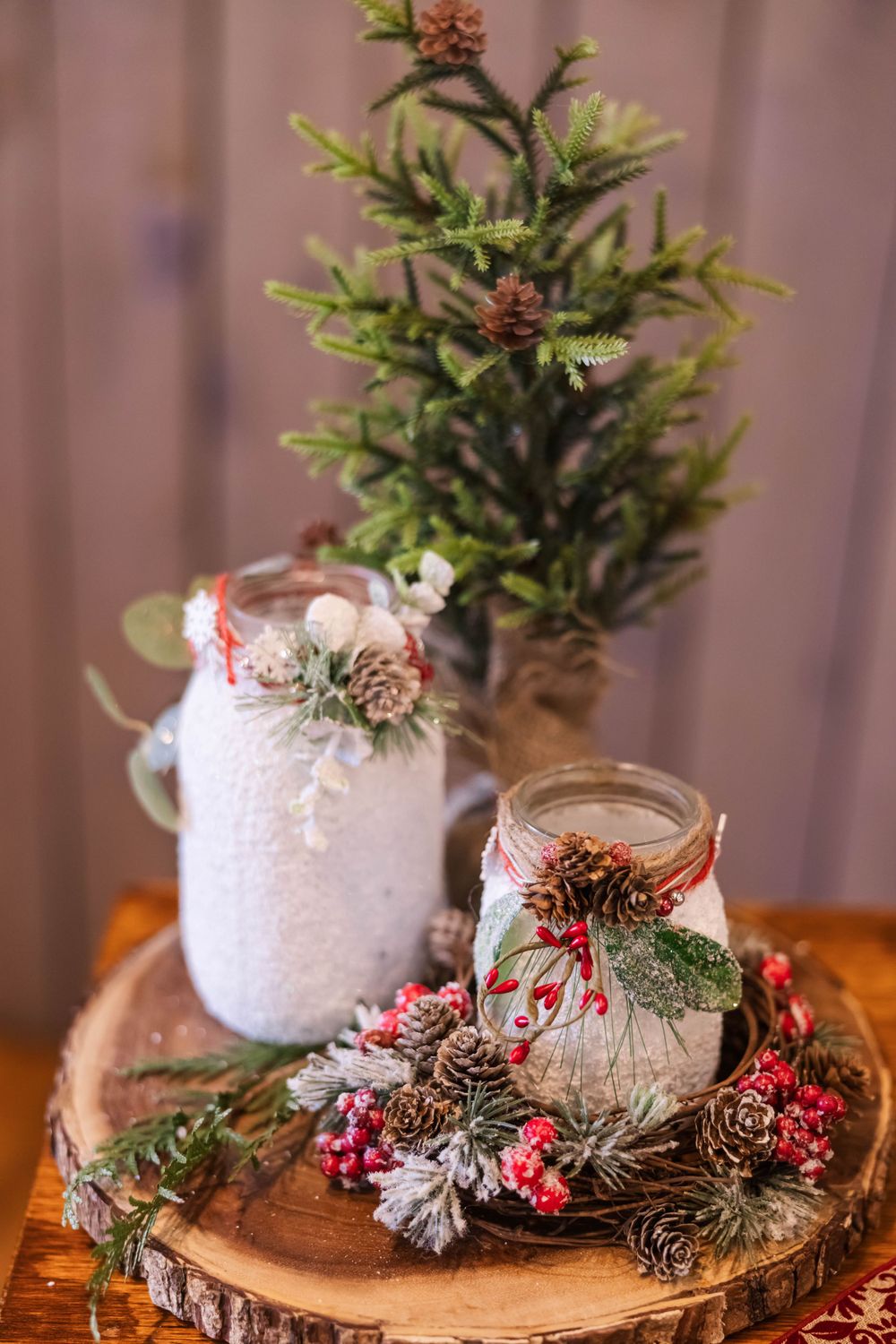 Festive winter centerpiece with mason jars, pinecones, and miniature Christmas tree on wooden slice.