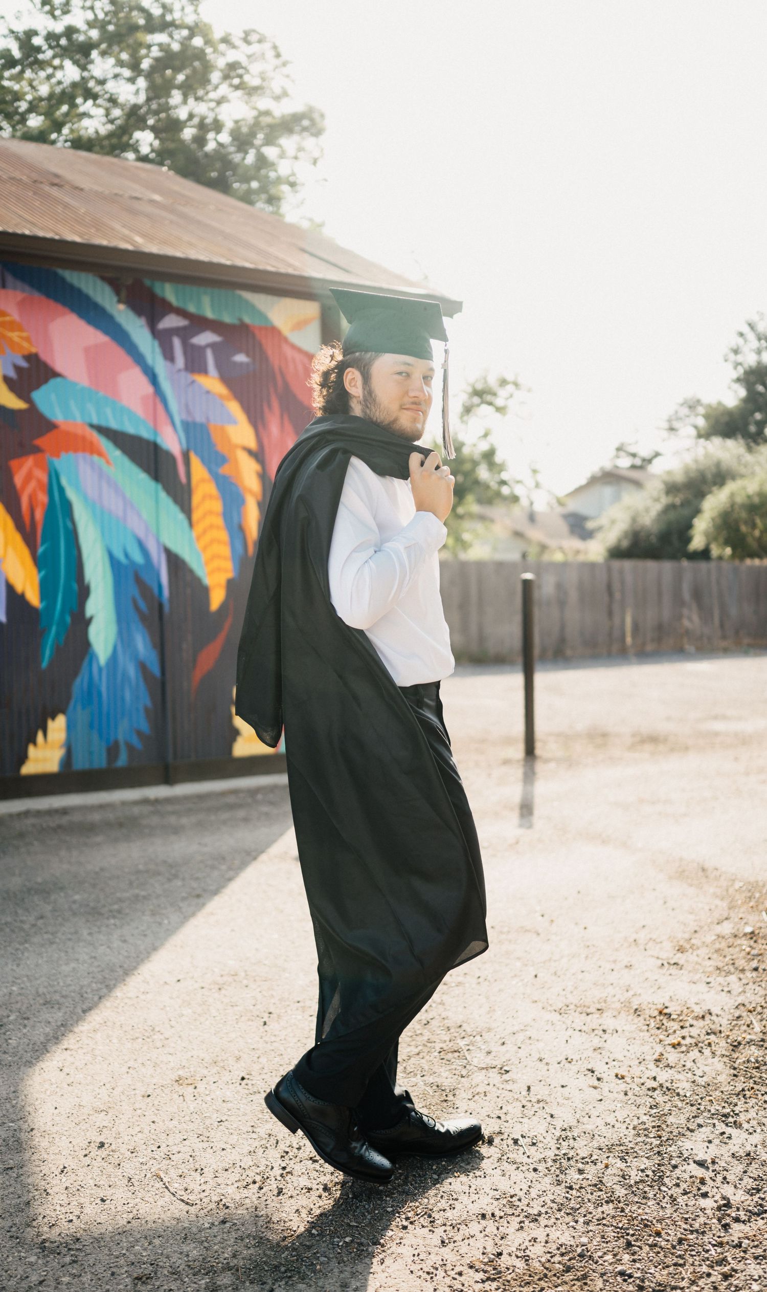 Graduate in cap and gown posing in front of colorful street art mural.