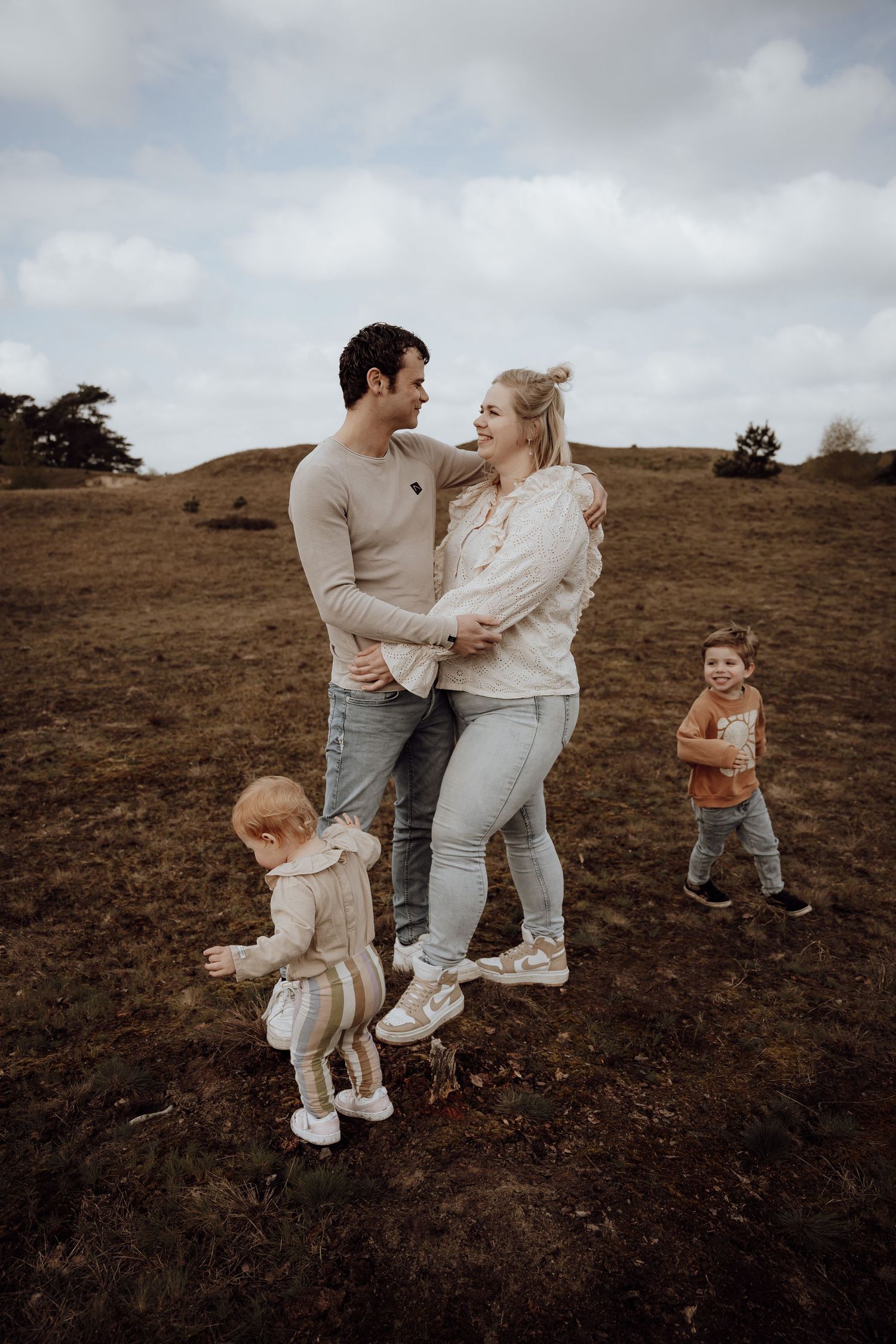 Man en vrouw hebben elkaar vast, kinderen rennen om heen heen. Vrolijke gezichten.