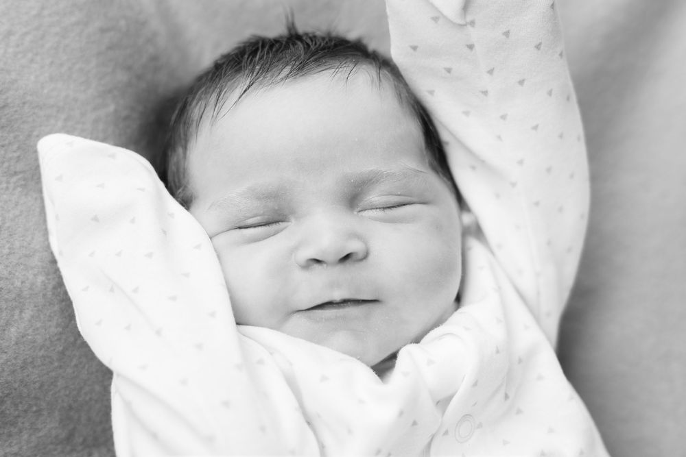 A peaceful sleeping newborn baby swaddled in soft white blankets in black and white.