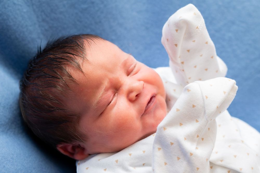 A sleeping newborn baby swaddled in white fabric against a white background.