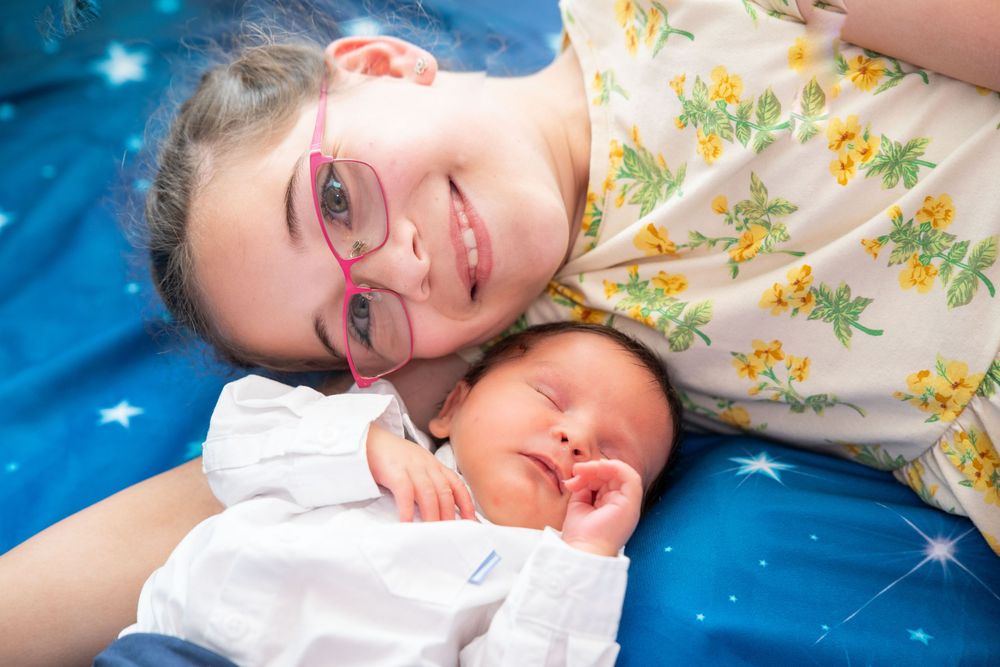 A peaceful moment with someone in a floral shirt resting with a sleeping baby on a blue star-patterned blanket.