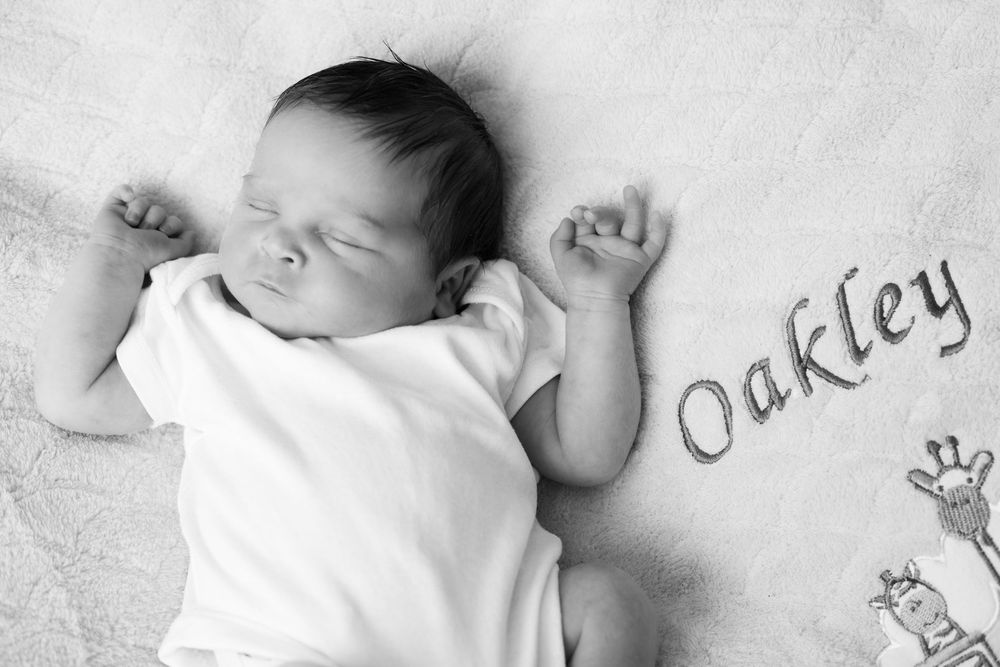 A sleeping newborn baby lies peacefully wrapped in white blankets on a soft white background.