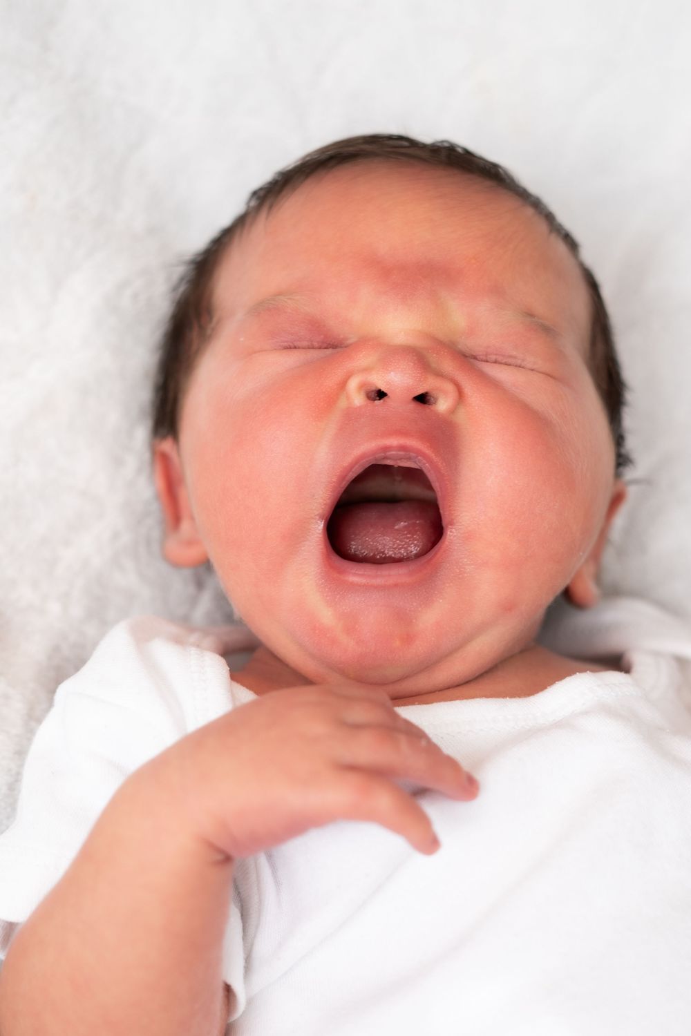 Four sweet photos showing a laughing newborn baby's face against soft white blankets.