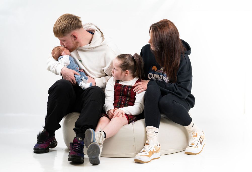 Family group sitting close together on white chair wearing casual hoodies.