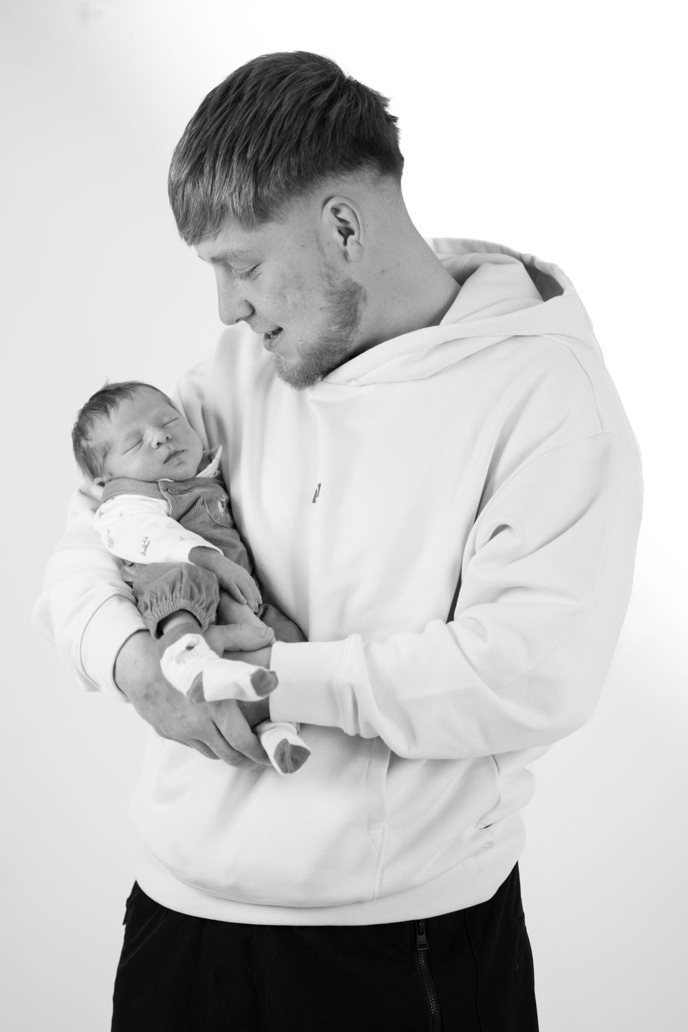 Black and white portrait of parent in white hoodie holding newborn baby.