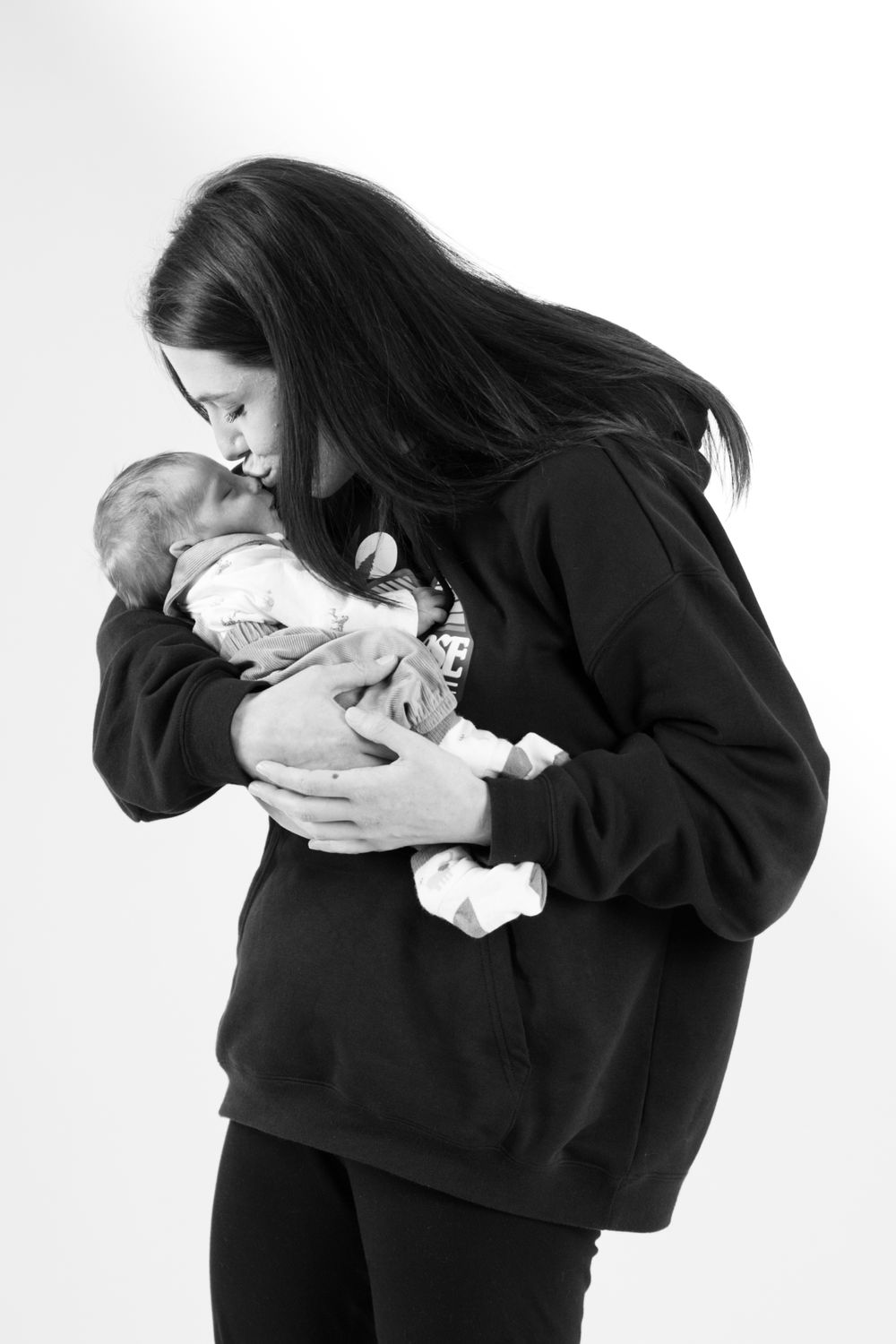 Black and white image of person in dark hoodie cradling sleeping newborn.