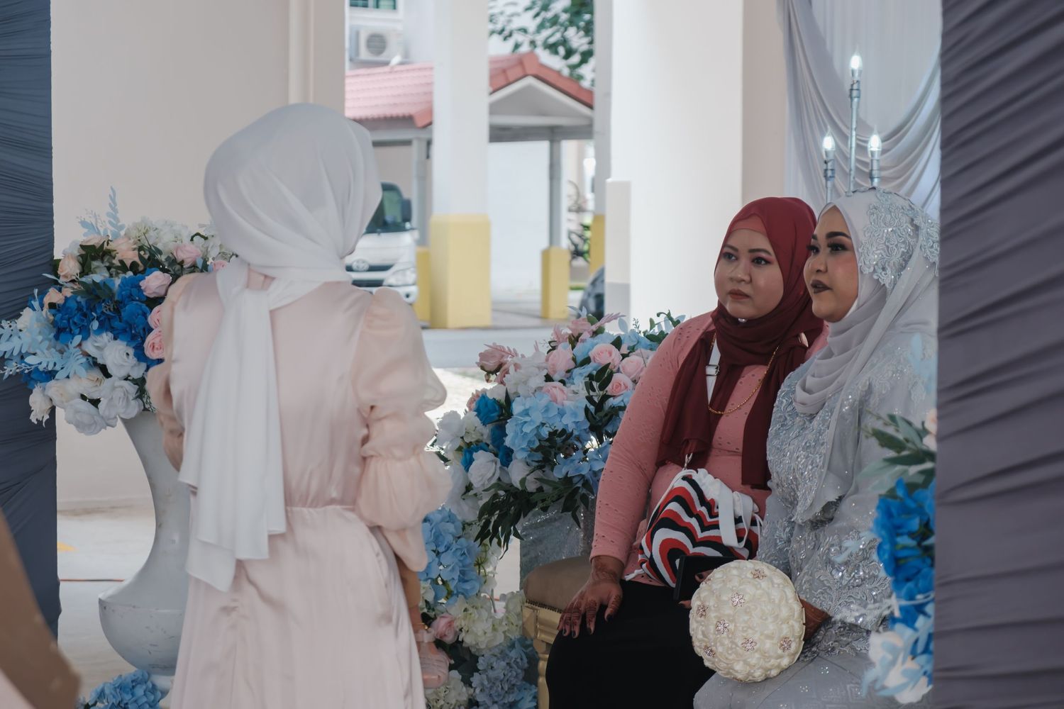Three women in hijabs conversing at an event decorated with blue and white floral arrangements.