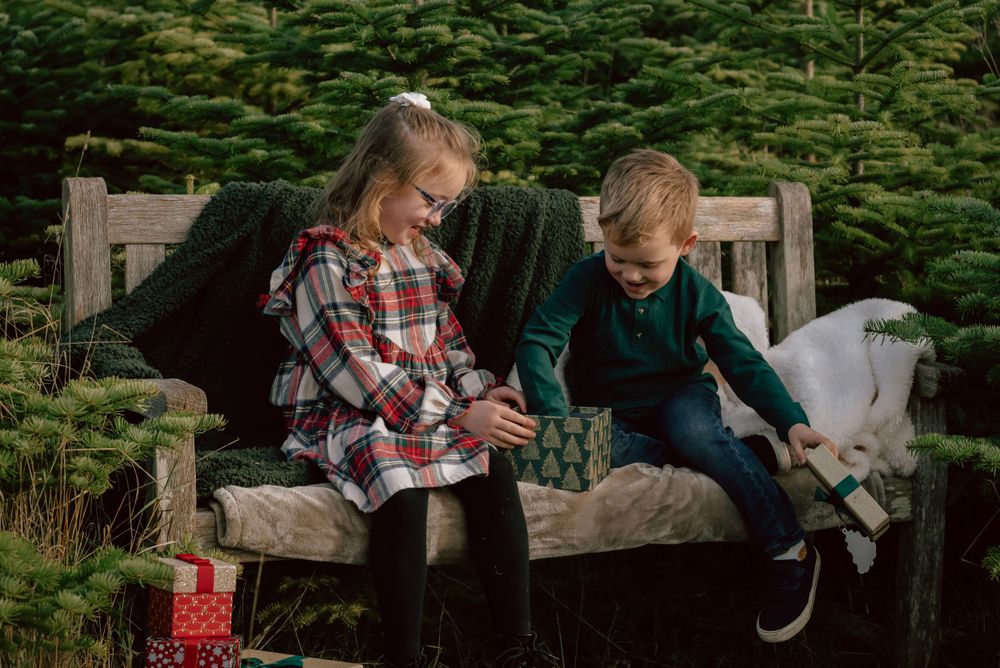 A brother and sister sit together opening present boxed that they have discovered. They smile as they observe what is inside.