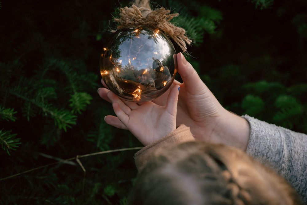 Two hands cradle a Christmas bauble. The reflection of a family can be seen on its golden glass.