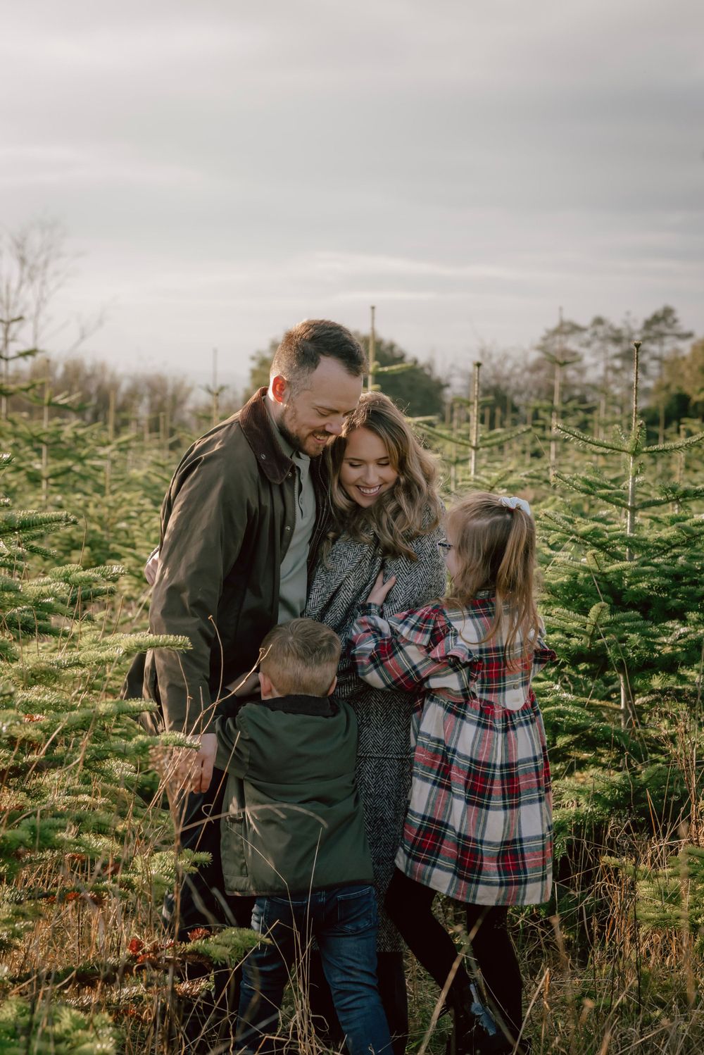 A family embrace on a Christmas tree plantation, the mother smiles as the children rush to greet her.