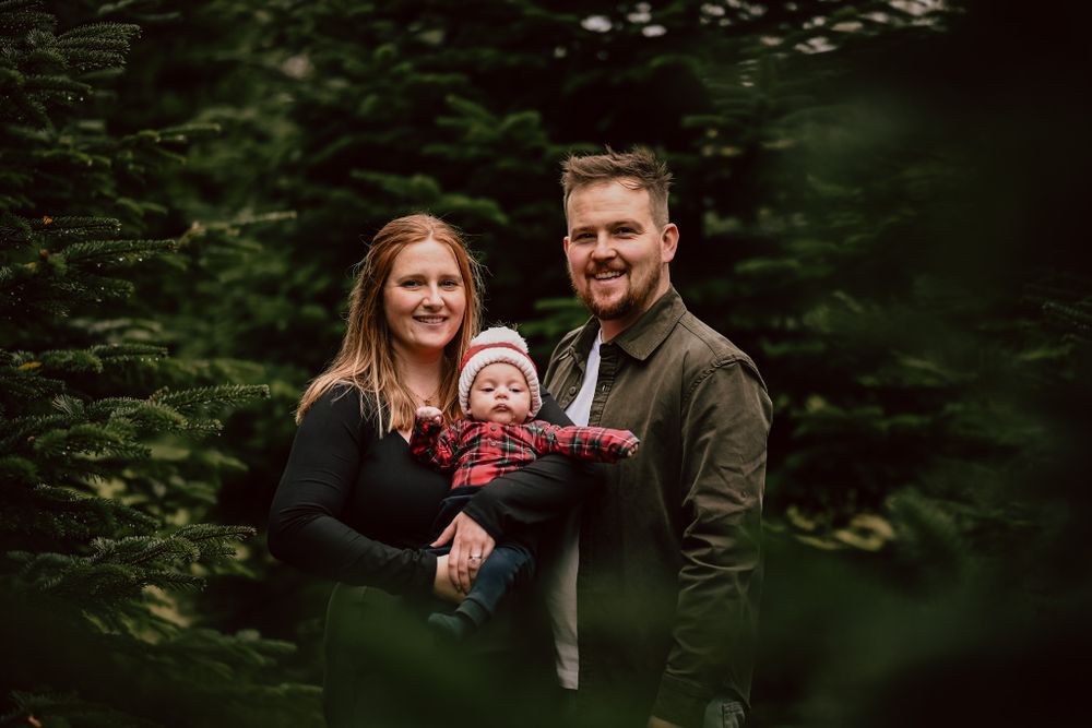 a family pose together amongst the christmas trees in December