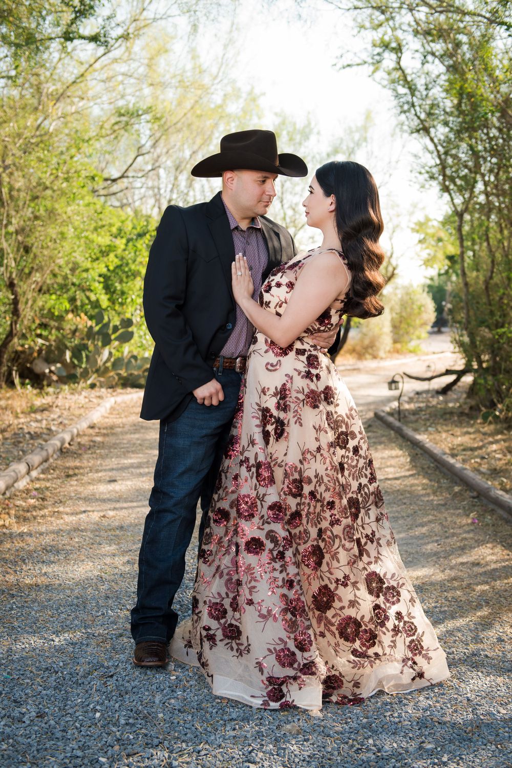 Romantic couple in western wear and floral dress pose on a garden path.