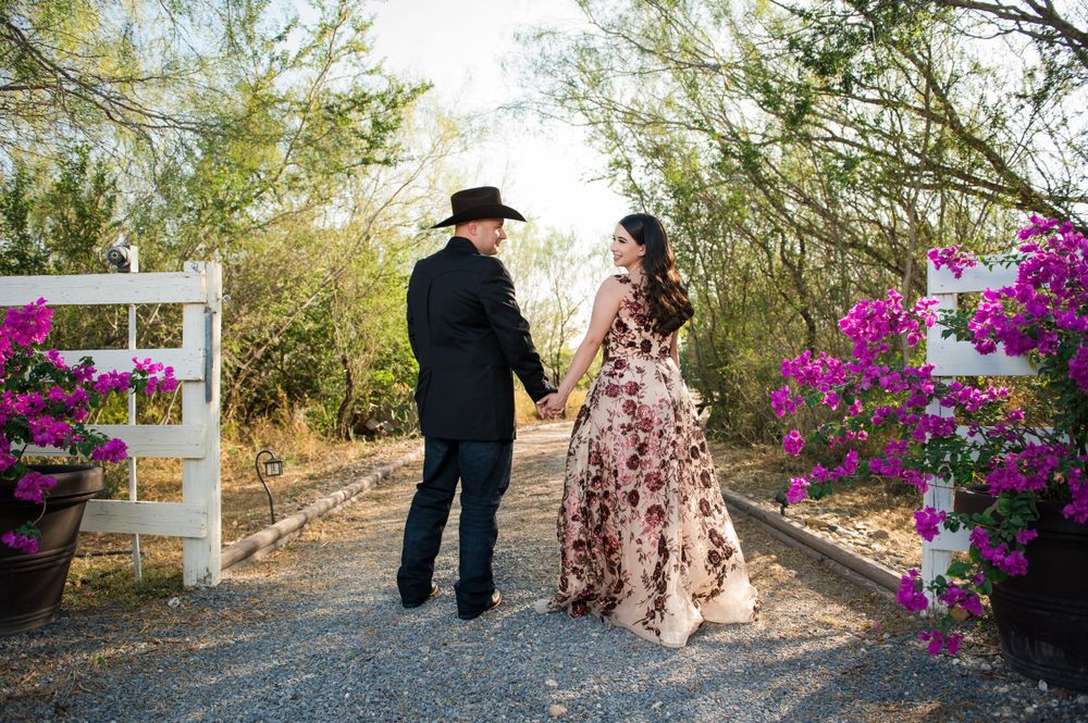 Couple walking hand in hand along garden path with blooming pink flowers and white fence.