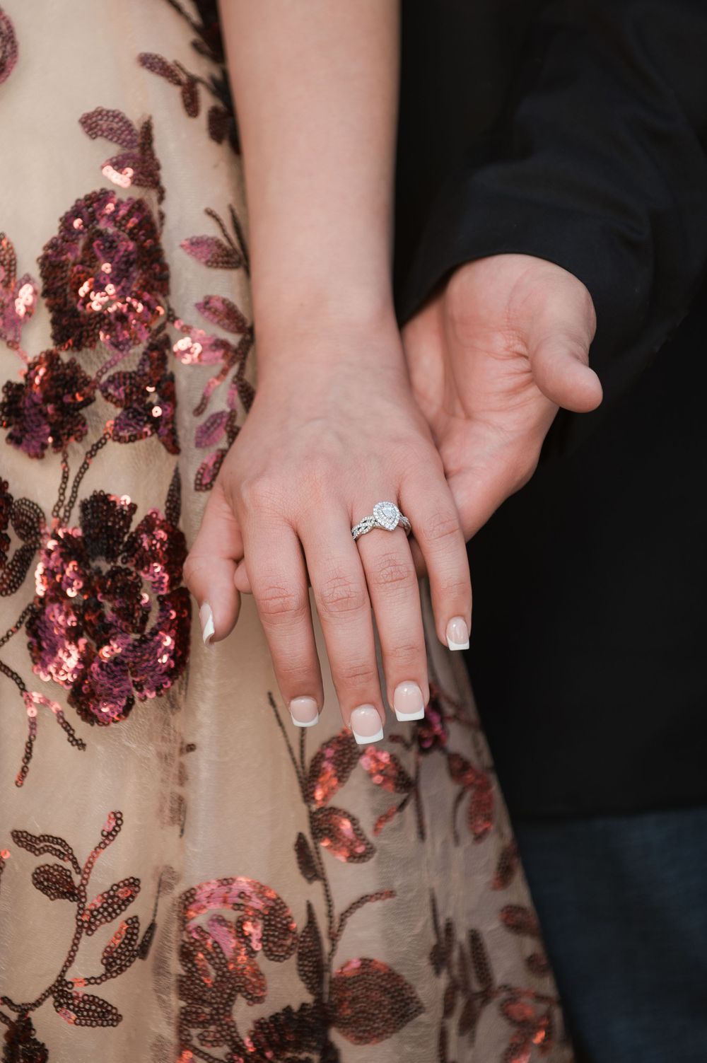 Close up of hands showing engagement ring against floral patterned dress fabric.