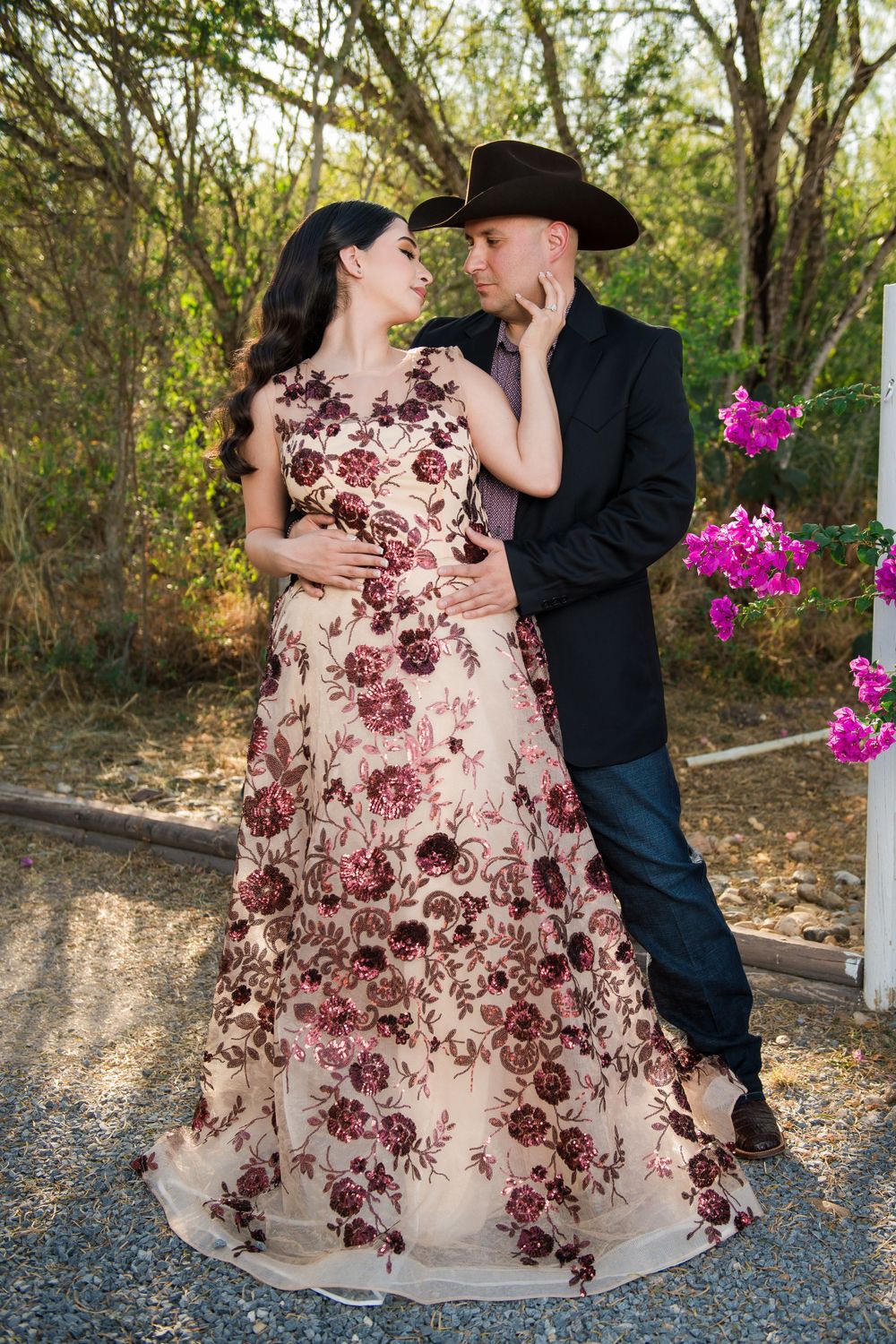 Romantic couple in formal attire share intimate moment on garden path with purple flowers.
