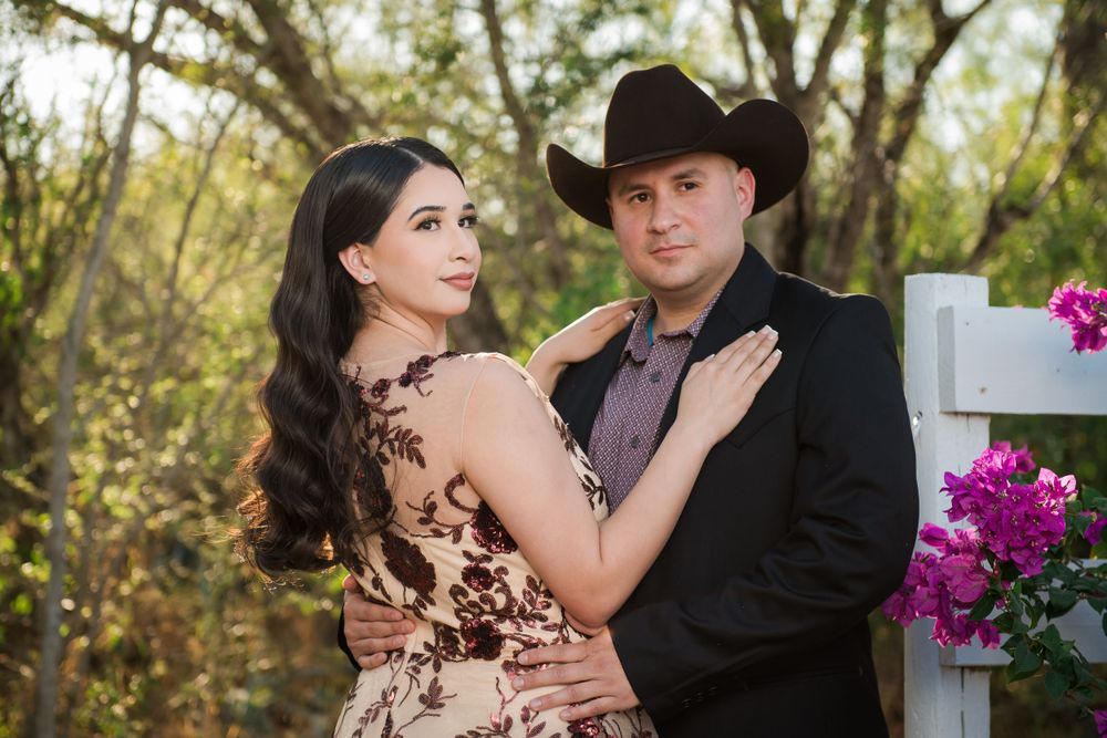 Couple poses by white fence and purple flowers in western formal attire.