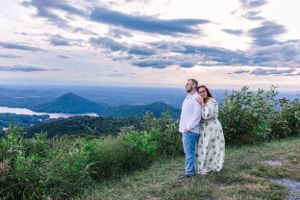 Couple standing together on mountain overlook with dramatic cloudy sky and valley views.