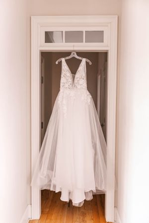 An elegant white wedding dress with lace details hanging in a doorway with transom windows.