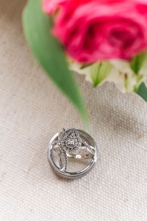 Elegant diamond wedding ring photographed with soft focus rose in background.