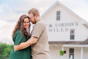 Happy couple embracing in front of rustic white farmhouse with signage.