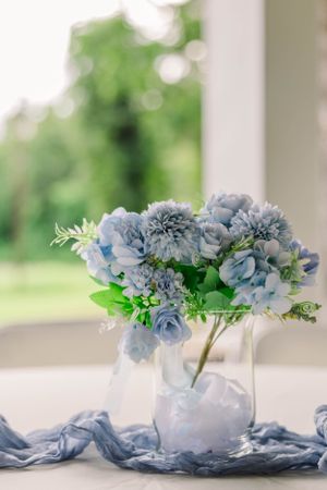 Elegant arrangement of blue hydrangeas and flowers in clear vase with flowing fabric.