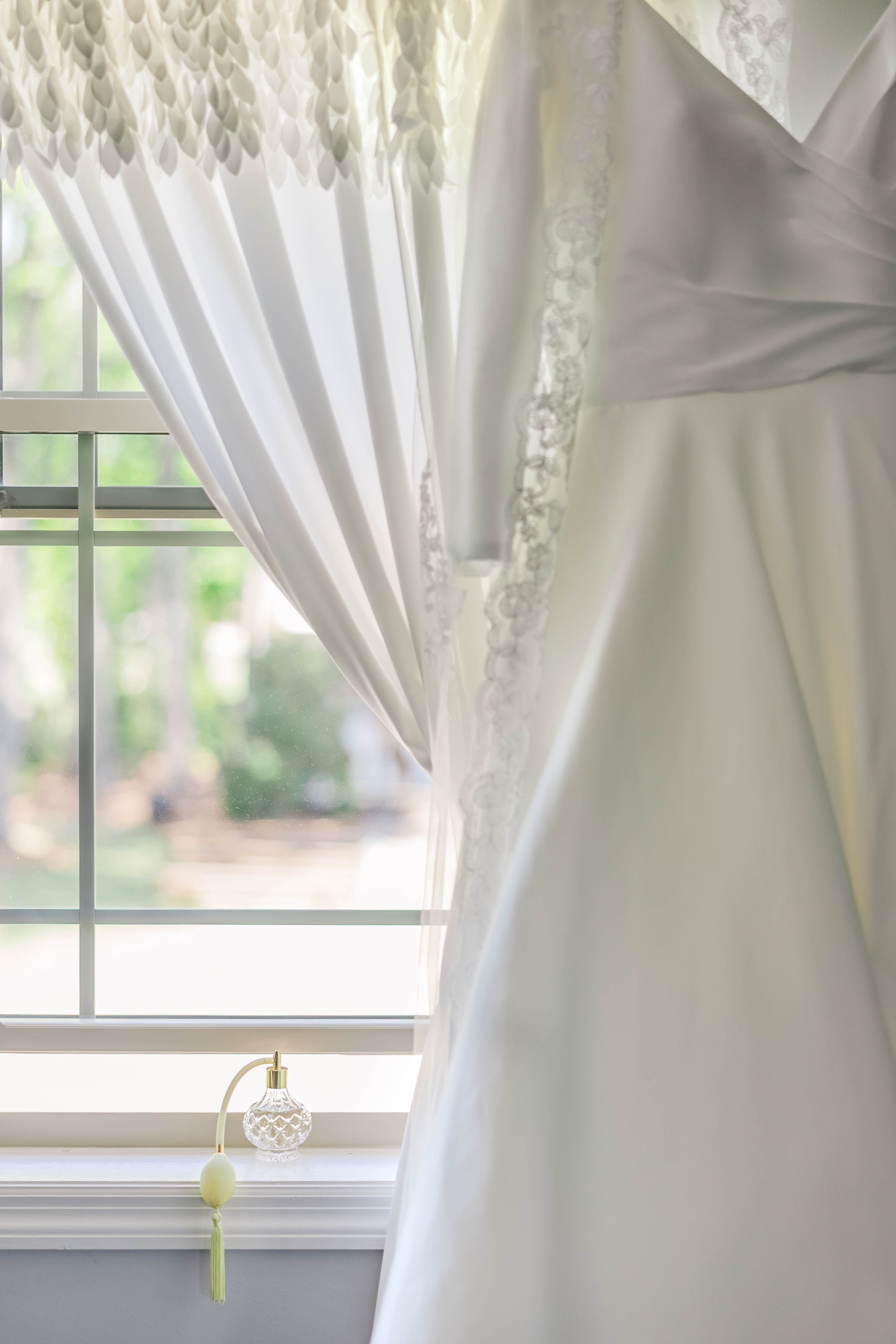 White lace wedding dress detail hanging by a window with natural light.