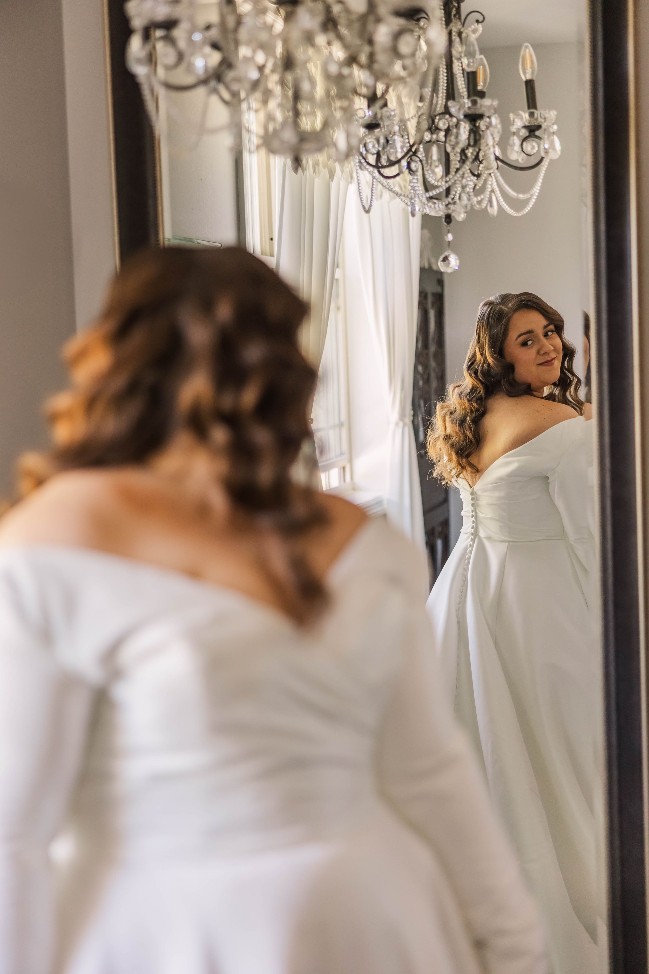Elegant room with chandelier and mirror showing wedding preparation reflections.