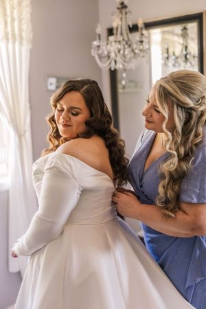 Wedding preparation scene with attendants helping with a white dress.
