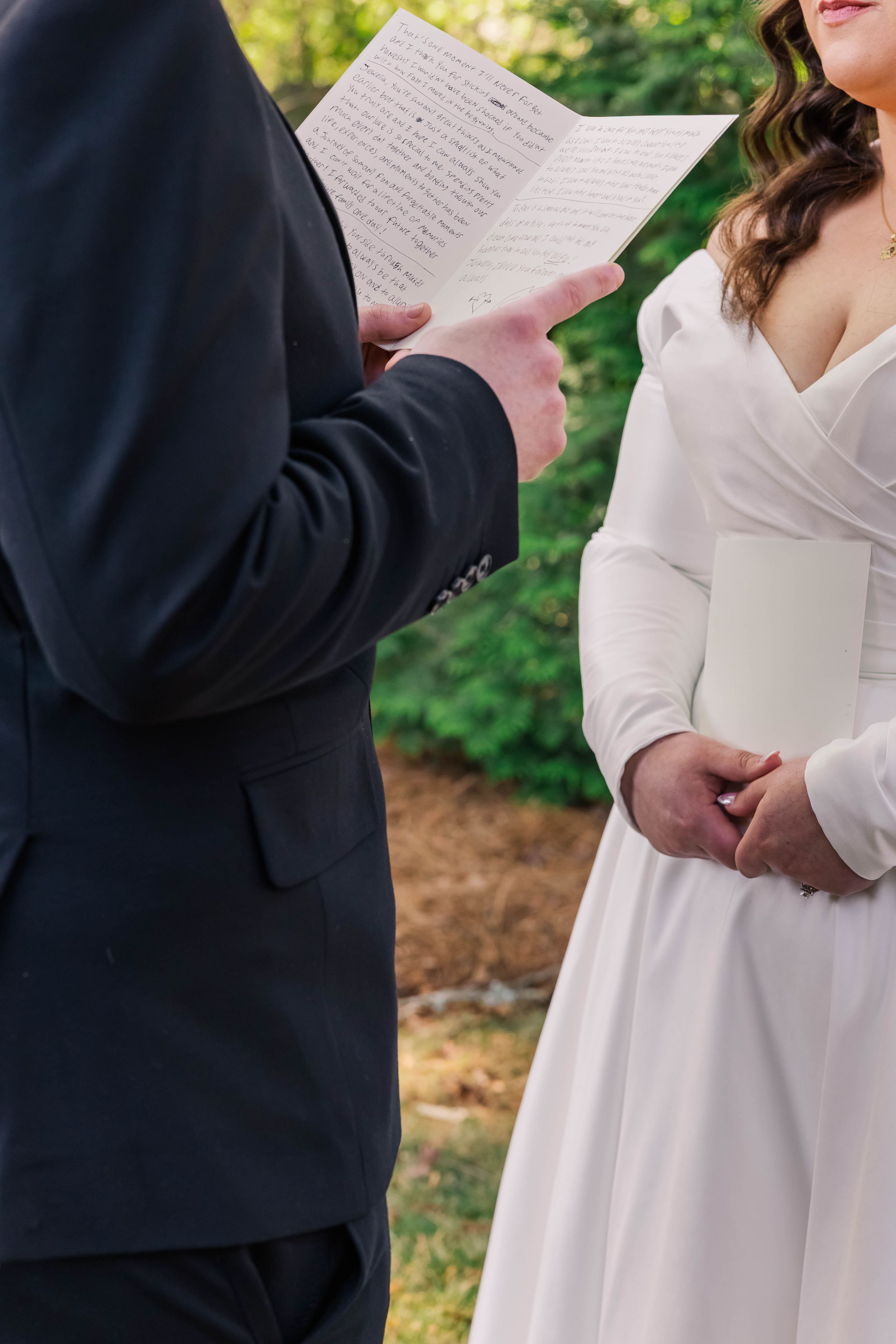 A close-up of hands holding wedding vows during an outdoor ceremony with greenery in the background.
