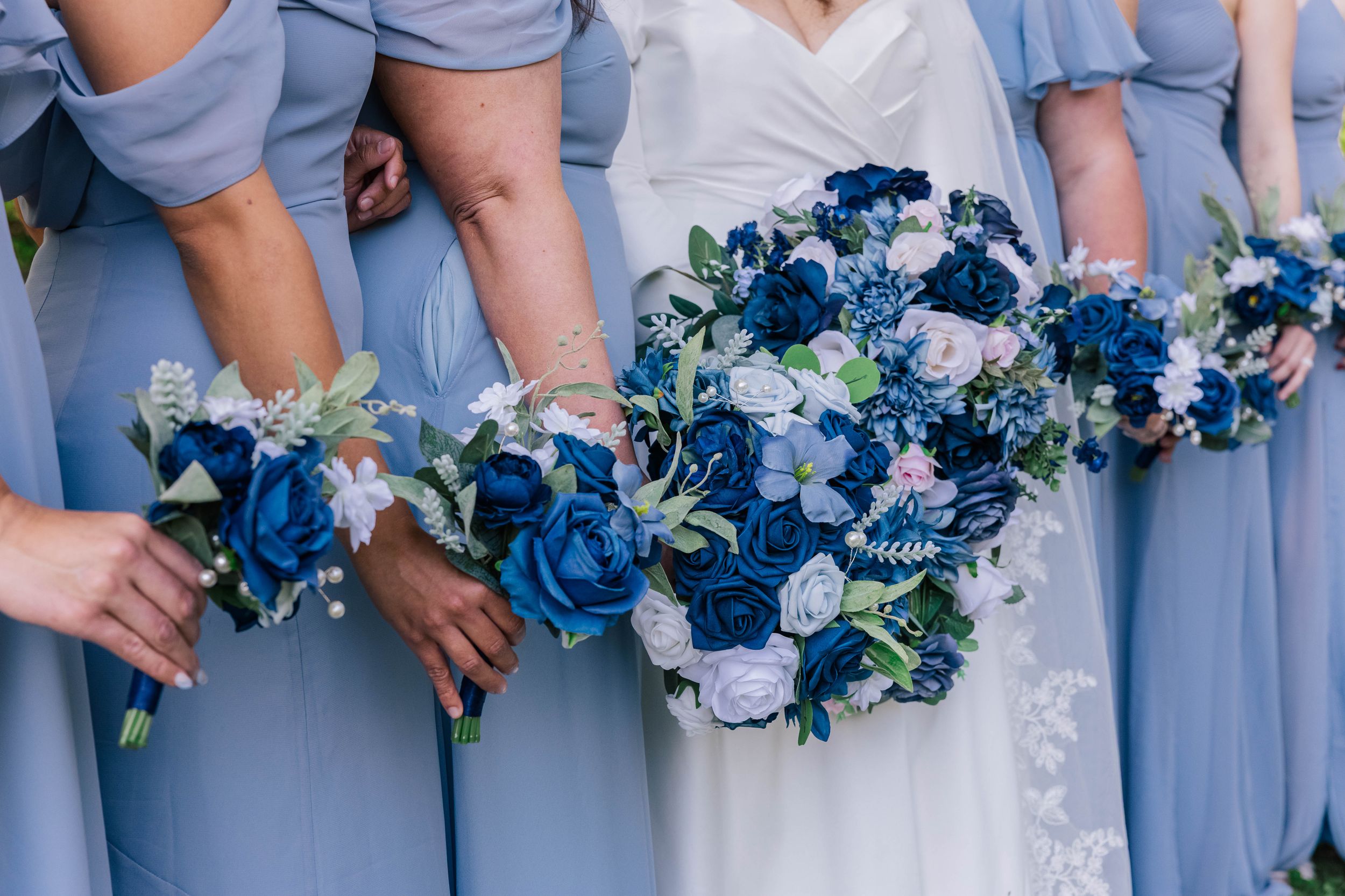 Bridesmaids in light blue dresses holding beautiful blue and white floral bouquets.