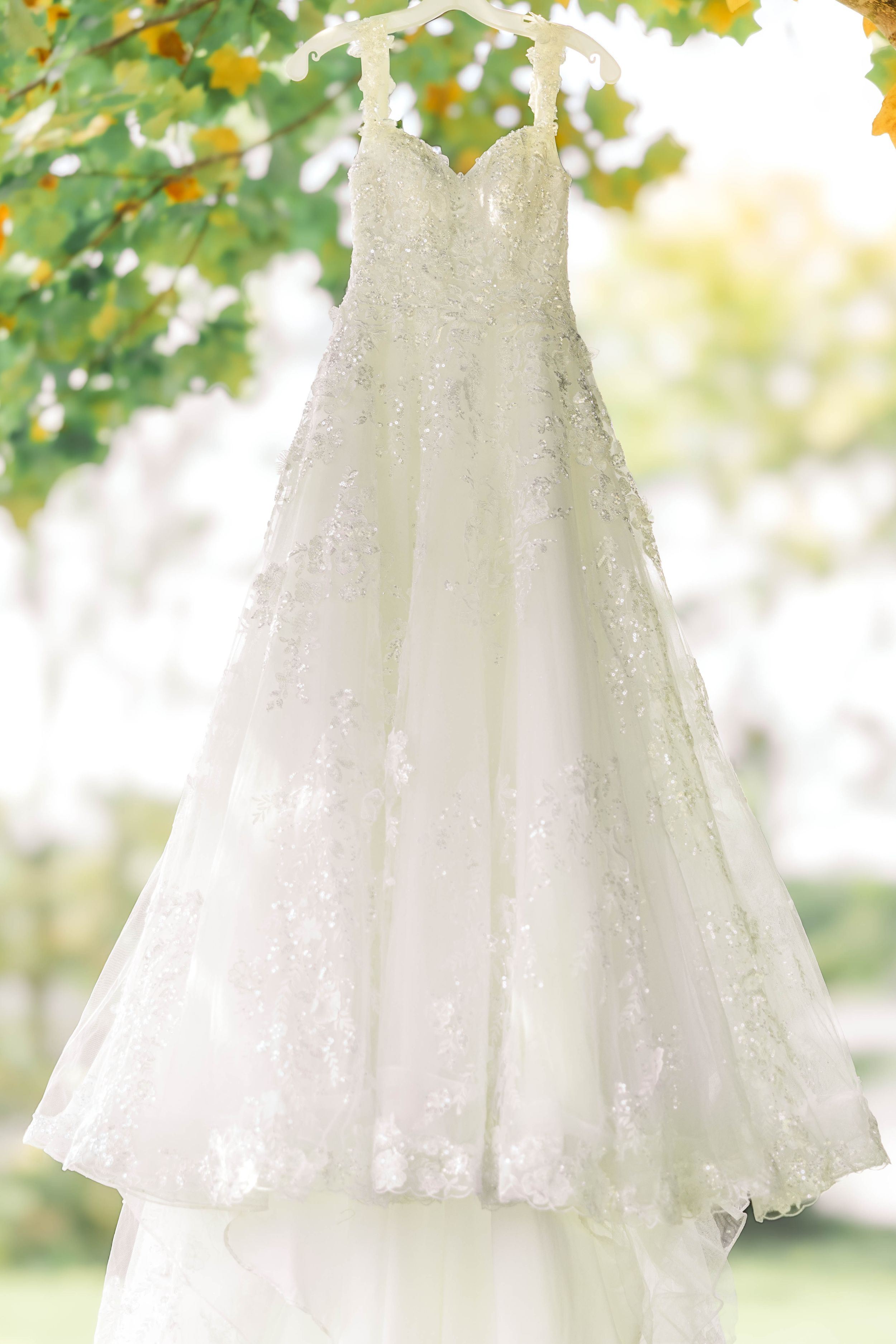 Elegant white lace wedding dress hanging outdoors against a soft bokeh background.