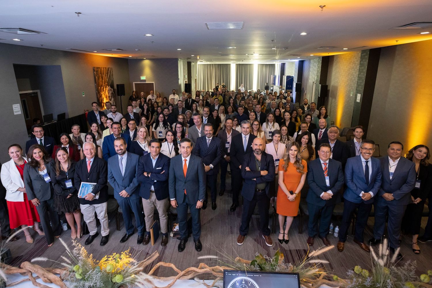 Large group of business professionals posing together at a corporate event in a modern conference venue.