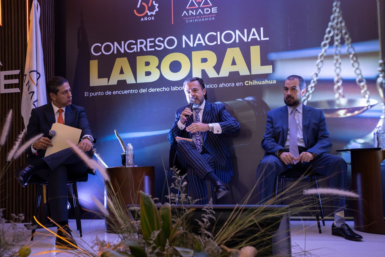 Three men speak at the Congreso Nacional Laboral event in Chihuahua, seated on stage before a branded backdrop.