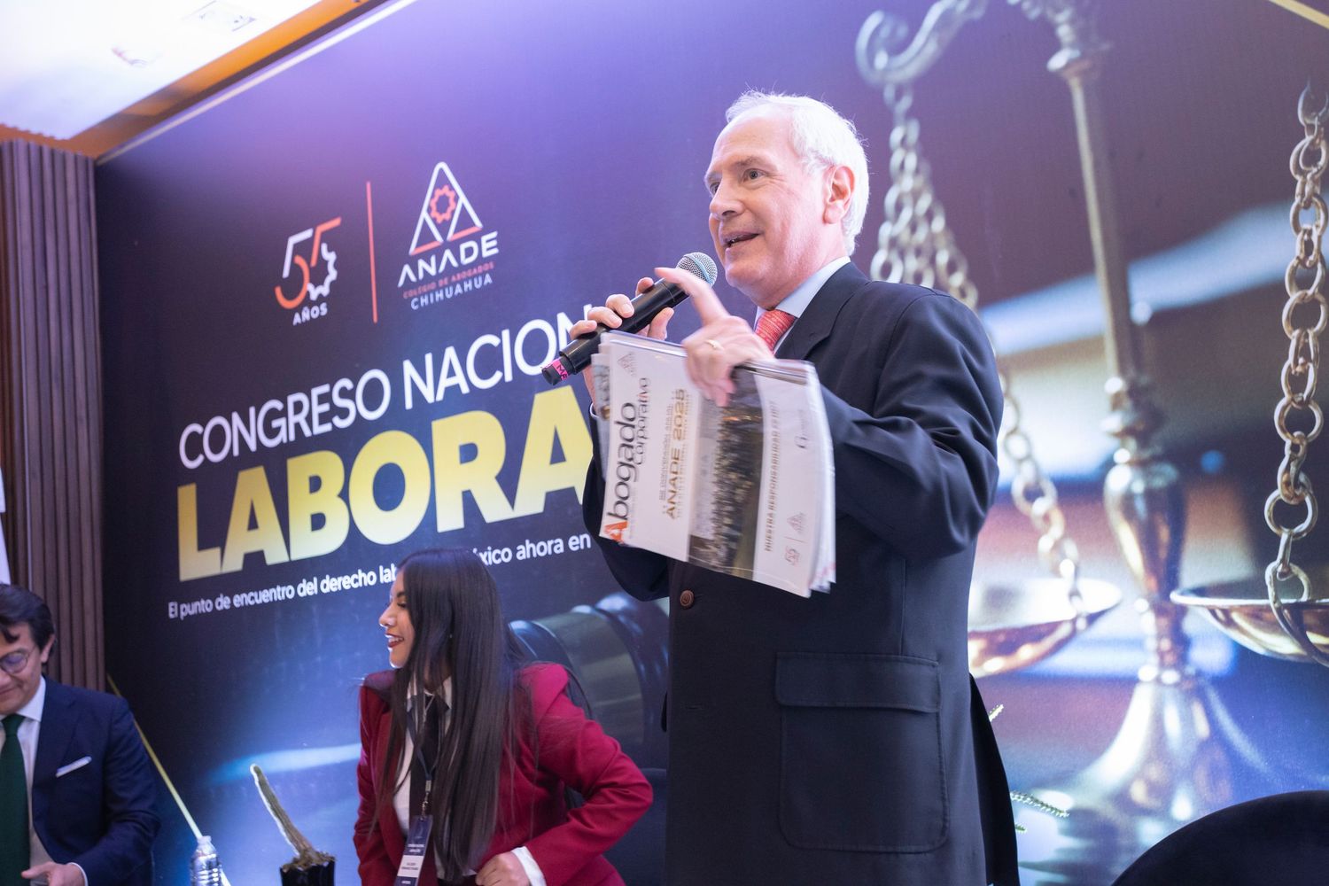 Speaker at Congreso Nacional Laboral event holds newspaper at podium, with scales of justice backdrop.