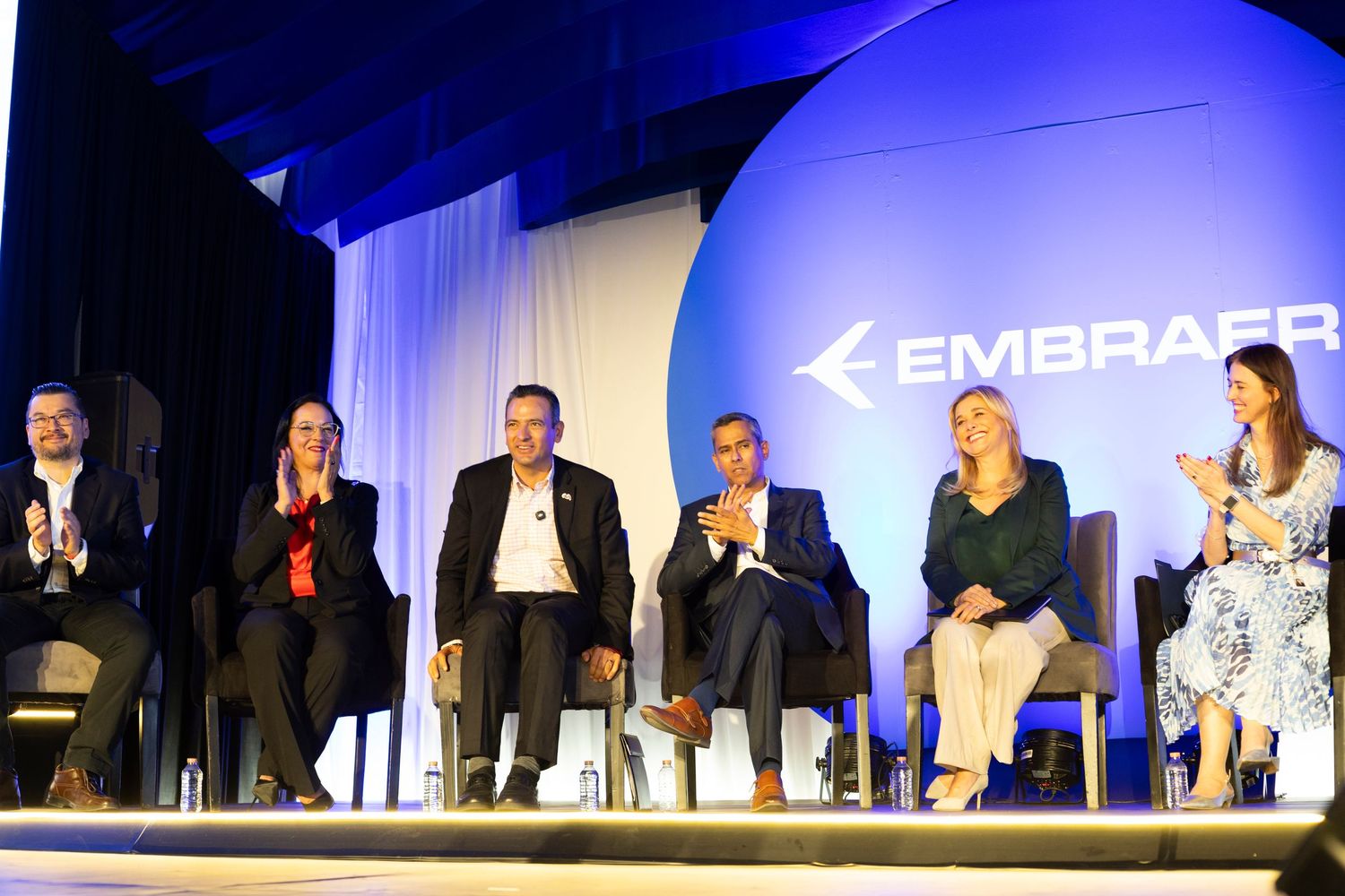 Embraer panel discussion with six executives seated on stage at a corporate aviation event.