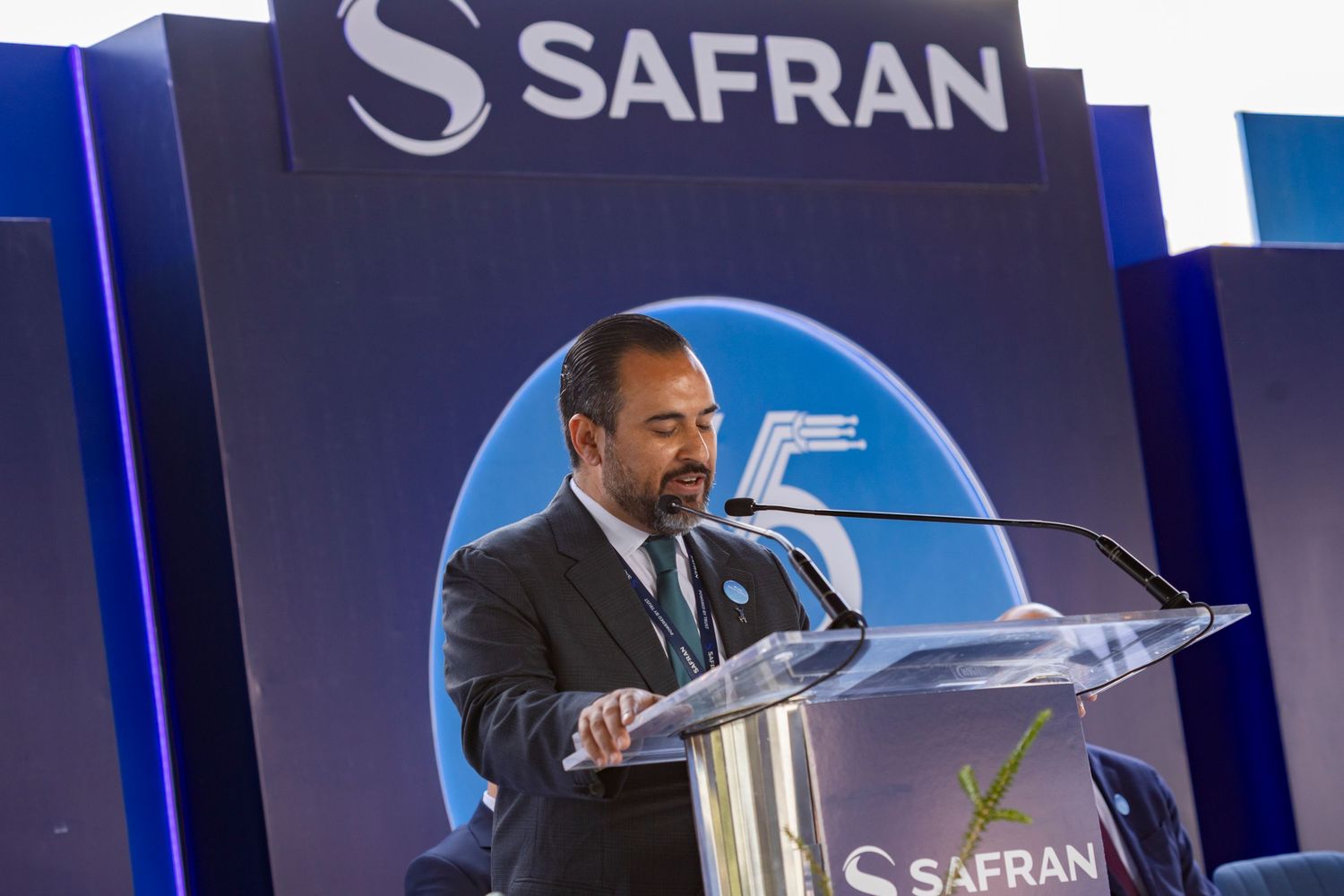 A man in a suit speaks at a Safran podium during a corporate event with the Safran logo displayed behind him.