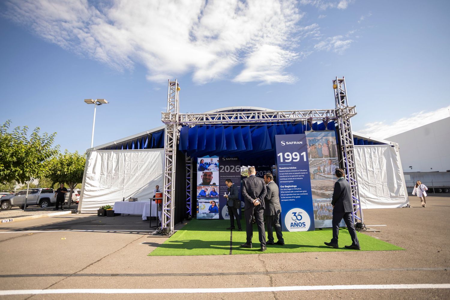 Two people stand on green turf in front of a branded 1991 anniversary stage display at an outdoor corporate event.