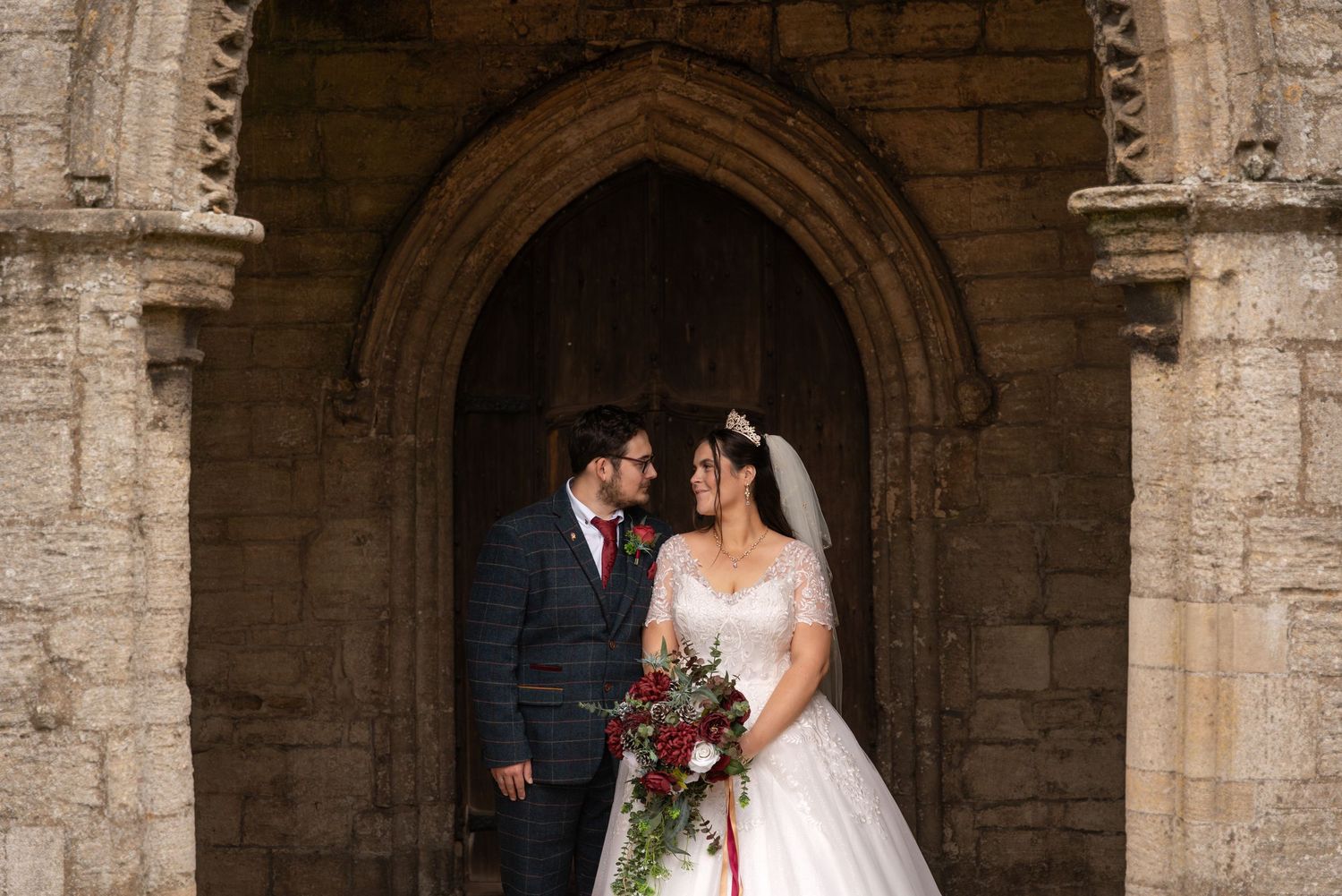 A bride and groom share a romantic moment under stone archways at a historic church or monastery.