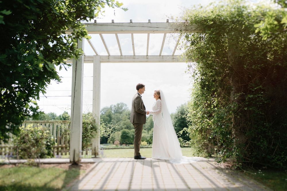 Couple standing under a white pergola surrounded by lush garden greenery.
